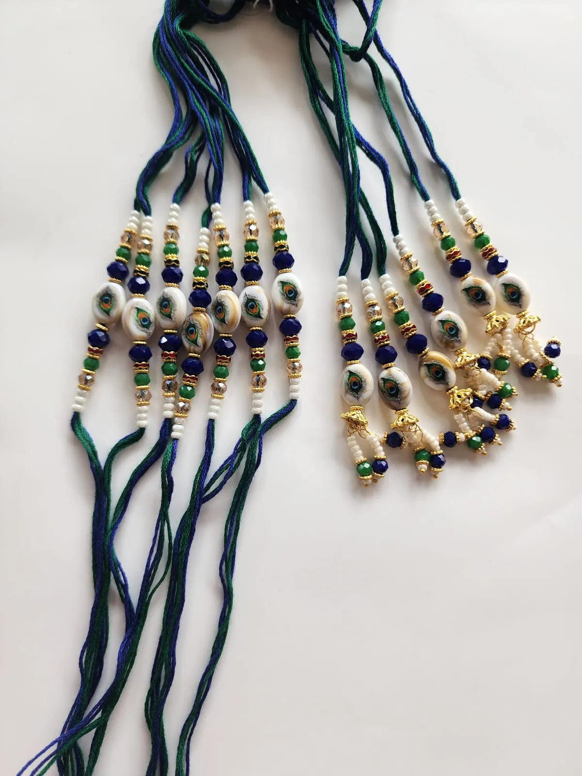 A set of traditional Hindu Lakshmi beads on dark blue and green cords, featuring white and green marbled beads, blue glass beads, and gold-plated trinkets on a plain white background.