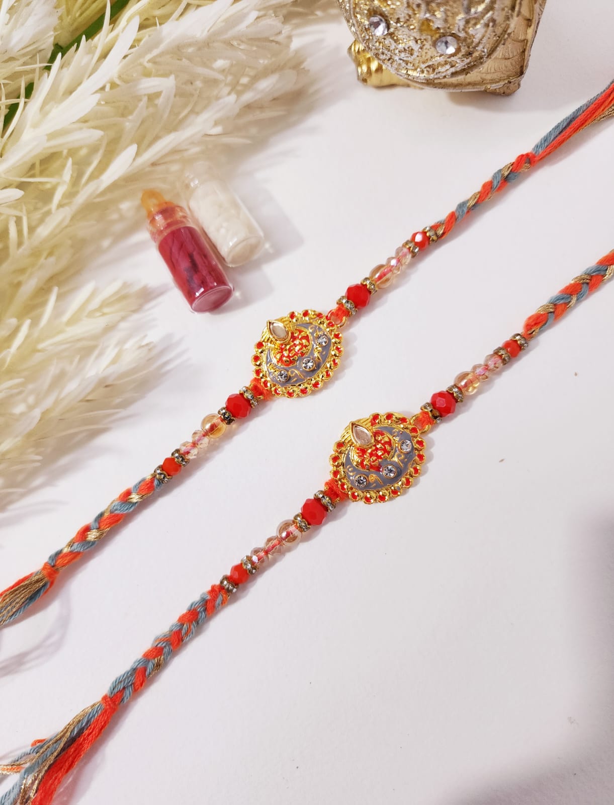 Two Hindu prayer beads, or 'rakhi', with intricate orange and gray designs, displayed on a white surface with decorative elements in the background.