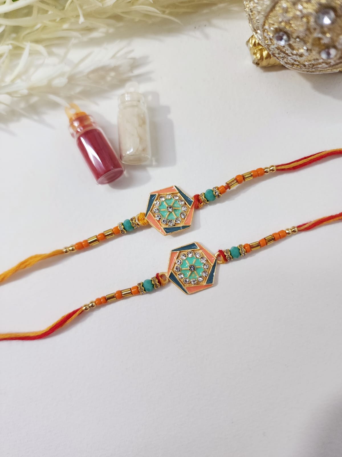 Two colorful designer rakhis with intricate patterns and embellishments placed on a white surface, accompanied by a small decorative item.