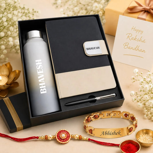 A Rakhi bandhan gift set in a black box, featuring a matte gray water bottle, a black and beige notebook with a pen, and a gold Rakhi bracelet engraved with 'Abhishek'. A matching gold 'Bhavesh' bracelet and a red thread Rakhi are also displayed in front on a beige background decorated with white flowers and gold lotus props.