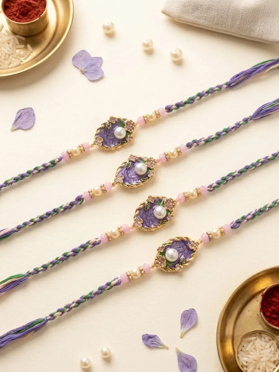 Four purple and green braided thread rakhi bracelets with gold-plated metal borders and central purple stone charms, each featuring a white faux pearl, arranged on a light beige surface with decorative props.