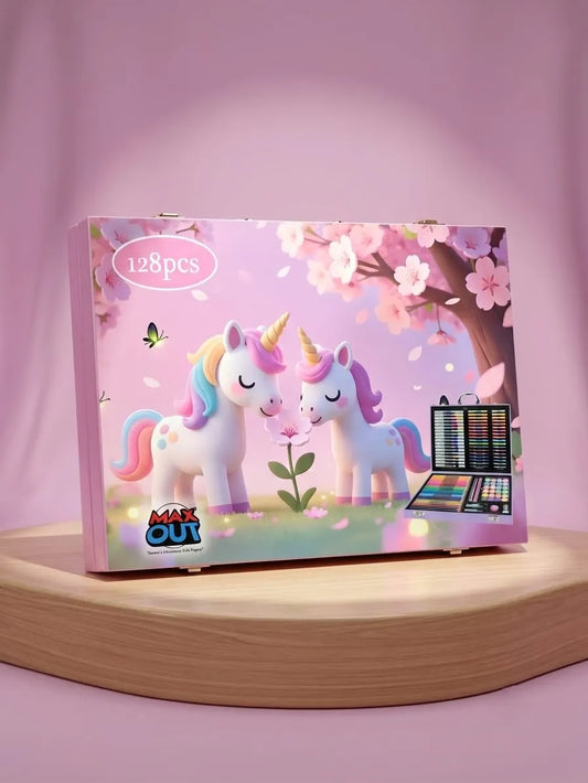 A pink toy makeup kit box labeled '128pcs' and 'MAKE OUT' sits on a curved wooden platform against a pink studio background. The box features an illustration of two unicorns under a cherry blossom tree, with a small makeup palette graphic shown on the front.