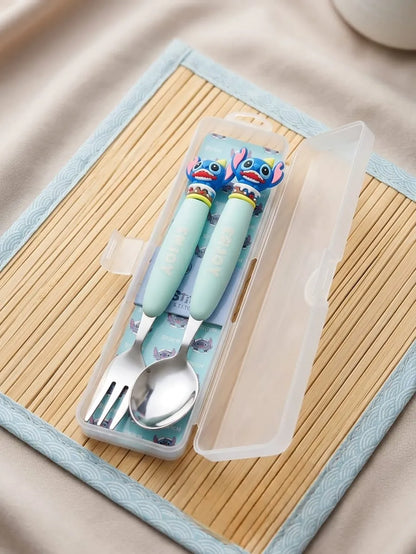 A children's stainless steel spoon and fork set in a clear plastic case, featuring mint green handles with cartoon character decorations, placed on a bamboo mat.
