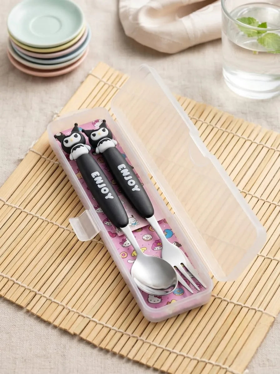 A small pink plastic utensil case holding a black-handled spoon and fork with cartoon owl faces and the word "ENJOY" on the handles, placed on a bamboo mat with stacked pastel plates and a glass of water in the background.