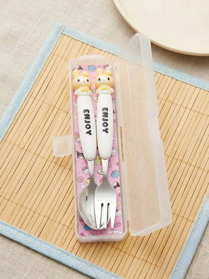 A set of two white baby utensils with cute cartoon character handles and 'ENJOY' printed on them, inside a clear plastic storage case with a pink patterned insert, placed on a bamboo mat.