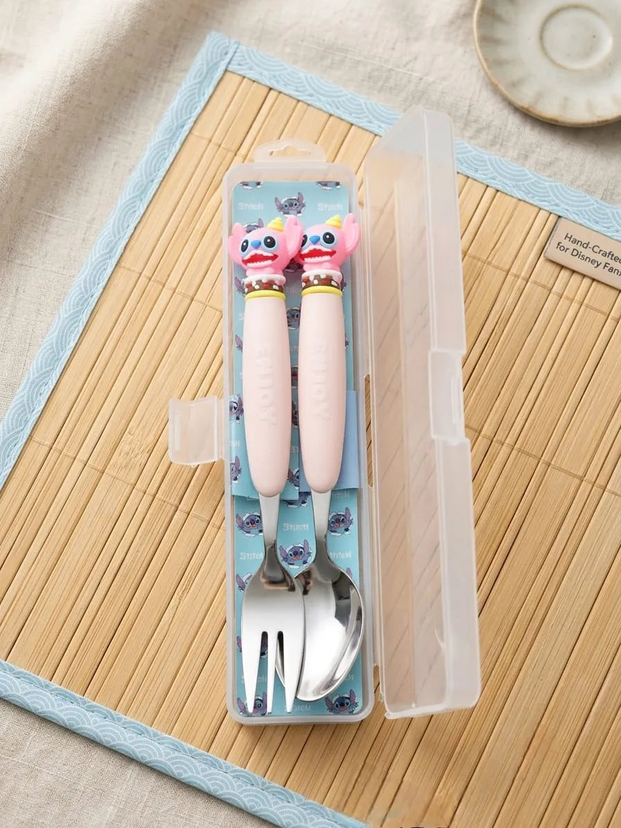 A children's stainless steel cutlery set in a clear plastic case, featuring light pink handles with cartoon character toppers and a blue patterned interior, displayed on a bamboo mat.