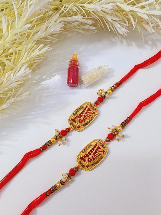 Two decorative rakhi bracelets with red thread and gold-colored embellishments, displayed alongside a small bottle of tilak (a traditional Indian tikka) on a decorative base.