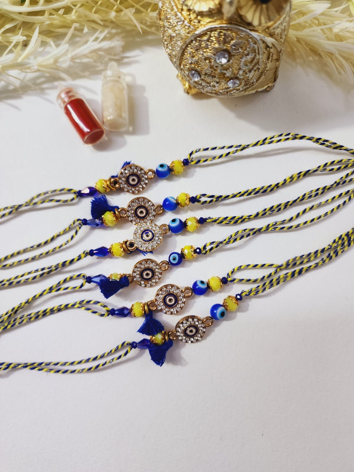 A Hindu ritualistic bracelet known as a Rakhi, featuring a combination of blue and yellow beads with a diamond-studded evil eye charm.