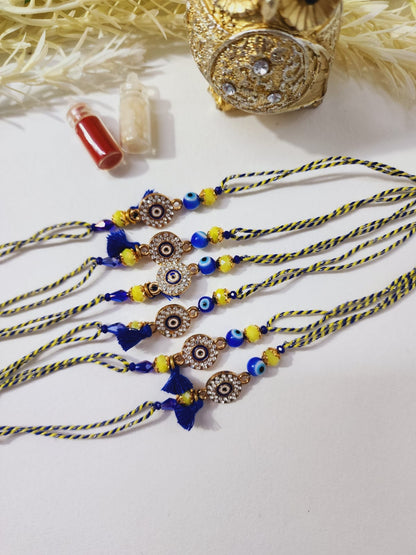 A Hindu ritualistic bracelet known as a Rakhi, featuring a combination of blue and yellow beads with a diamond-studded evil eye charm.