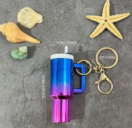 Blue and purple keychain light with measurements on a gray surface with shells and a starfish.