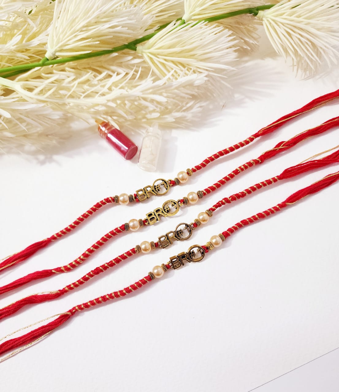Red beaded bracelets with gold clasps on a white surface with dried flowers.