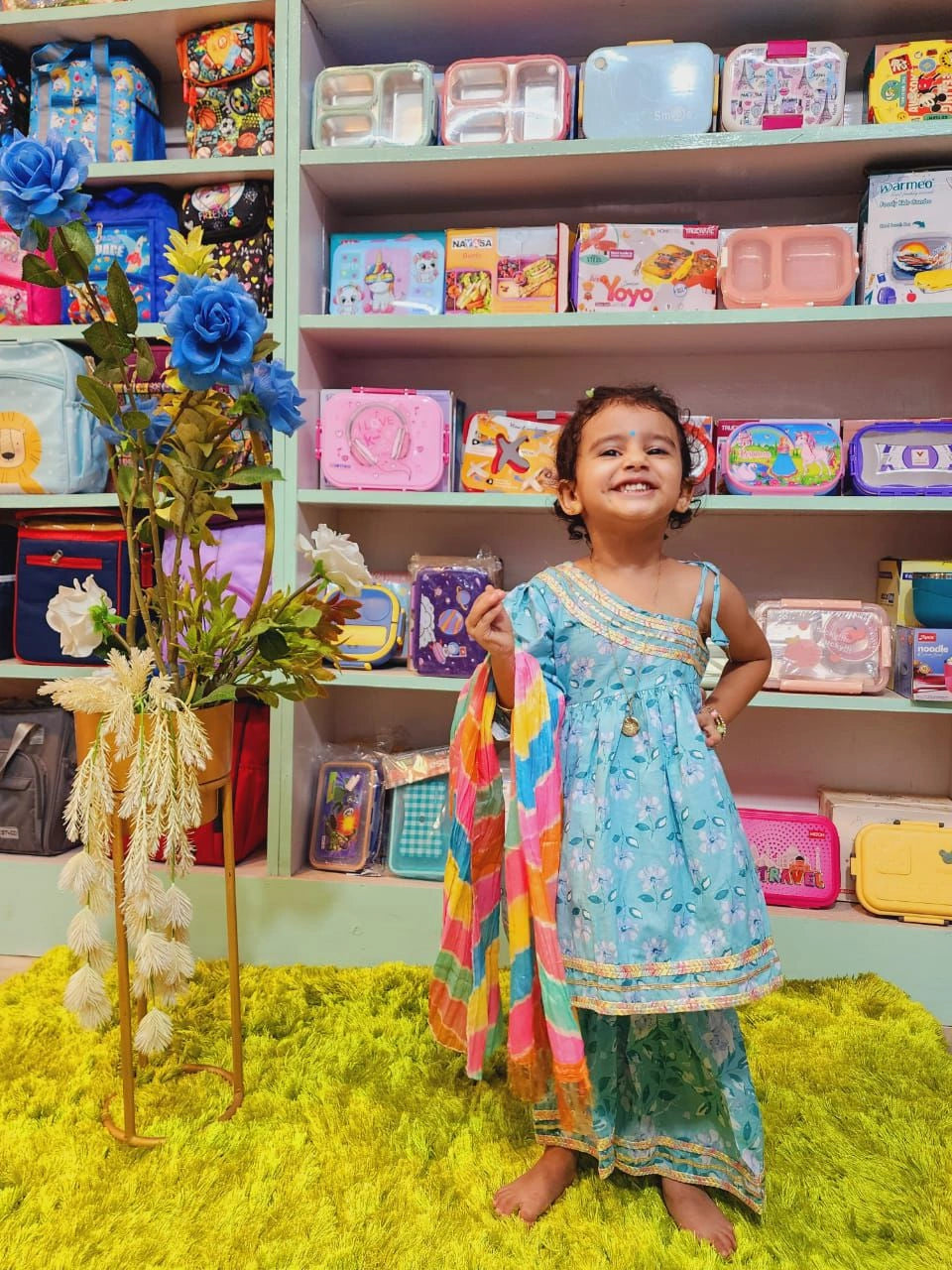 Child in a colorful dress standing in front of shelves filled with toys and products.