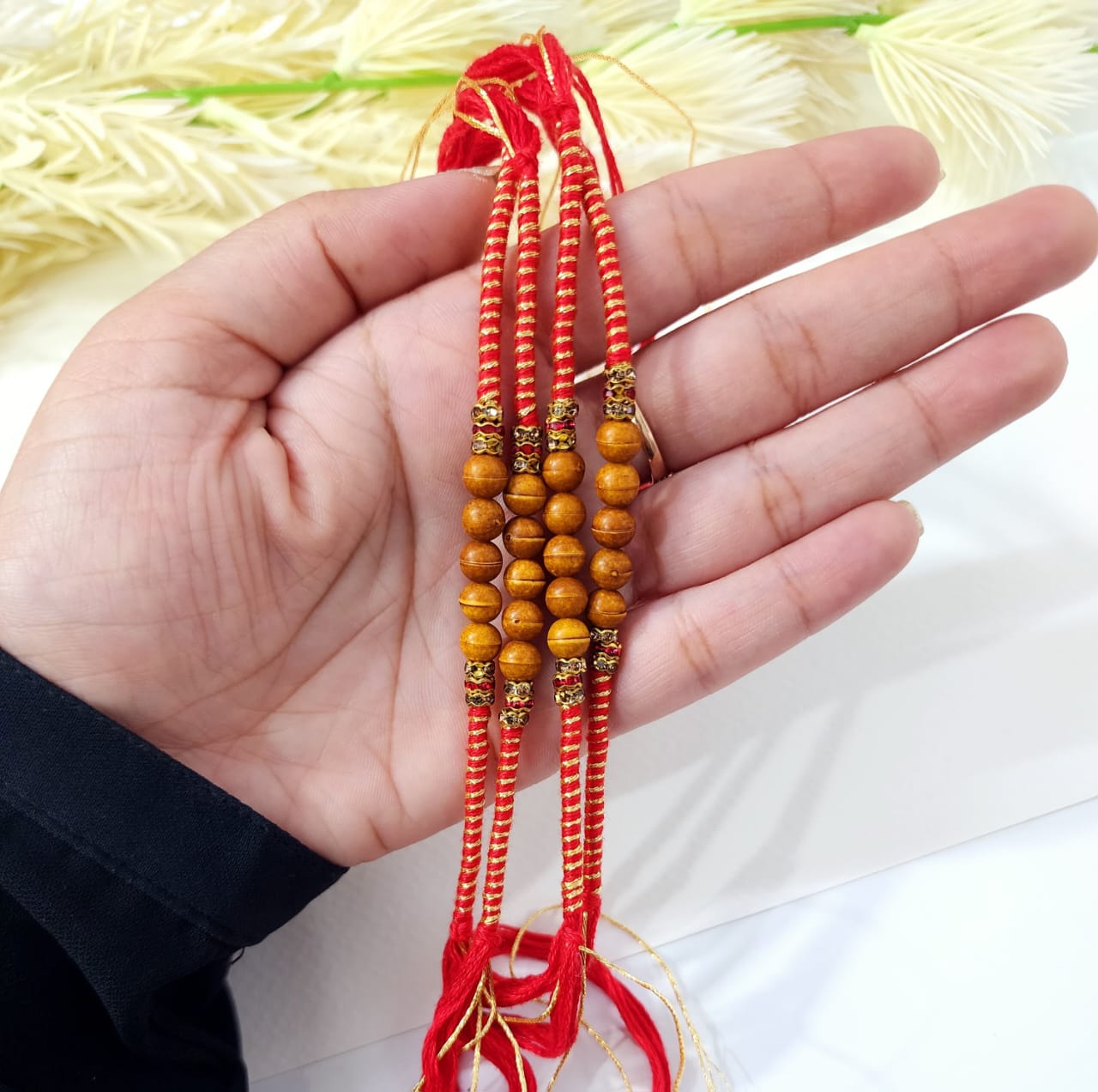 Hand holding a string of wooden beads with red thread against a light background