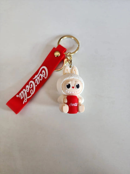 Coca-Cola keychain with a small character attached to a red strap on a light gray background