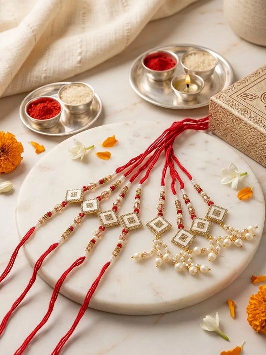 Four traditional Indian Rakhi wristlets with red threads, gold and white beads, and pearl-like drops, arranged on a round white marble platter with festive decorative props.