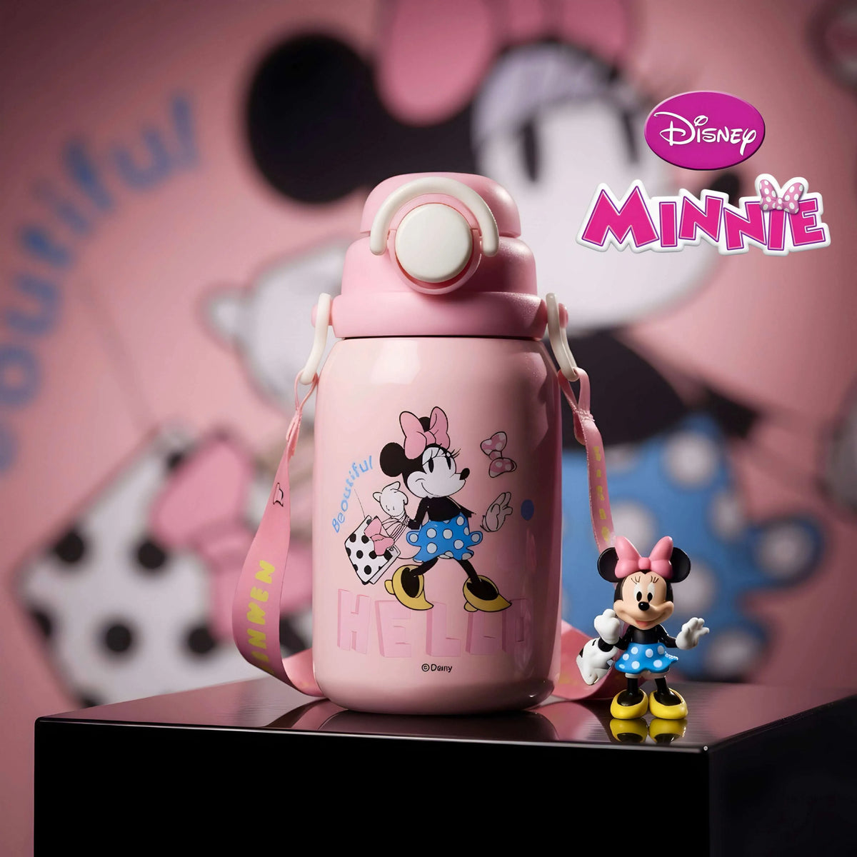 A pink Disney Minnie Mouse insulated water bottle with a matching pink shoulder strap, displayed on a black pedestal with a small Minnie Mouse figurine beside it. The background is a soft pink Minnie Mouse-themed backdrop with the Disney Minnie logo visible in the upper right.