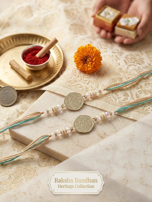 Two Raksha Bandhan traditional beaded wristlets with coin charms displayed on a cream patterned fabric alongside festive props including a brass plate with red powder, a marigold flower, and small gift boxes held by a hand. A label at the bottom reads 'Raksha Bandhan Heritage Collection'.