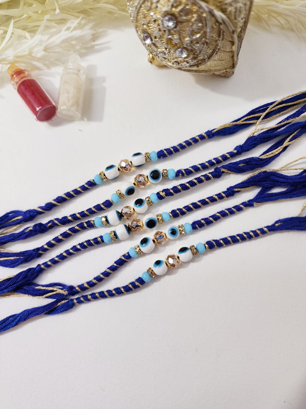 A collection of blue and multicolored thread rakhis with decorative elements and protective evil eye symbols.