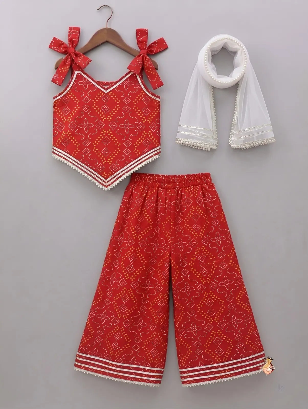 A three-piece children's outfit set displayed on a neutral gray background, including a red sleeveless top with bow shoulder straps, matching red patterned pants, and a white sheer scarf.
