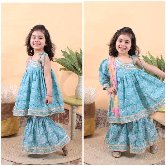 A girl wearing a blue sleeveless kurti sharara set with tie-dye dupatta, posing in two different angles against a backdrop with plants.