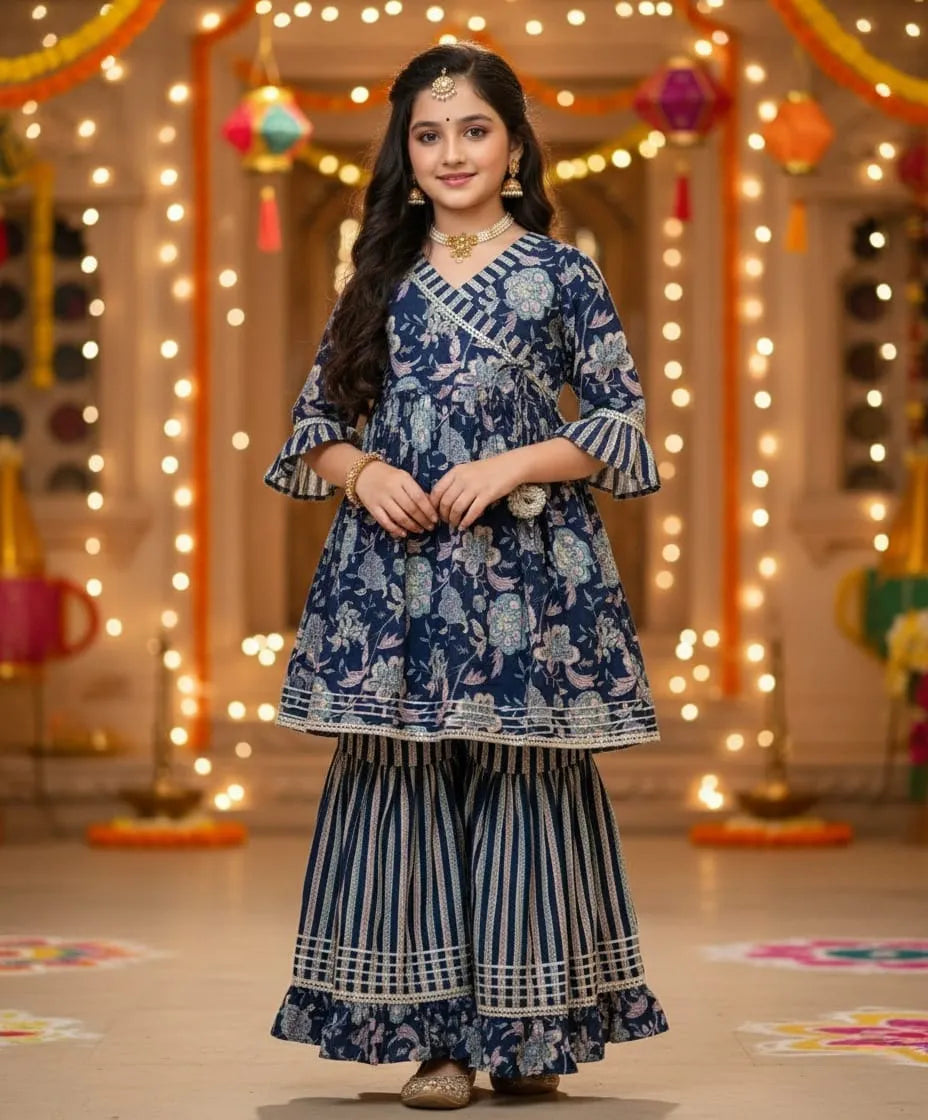 A woman modeling a navy blue and white printed traditional Indian outfit with wide-leg striped pants, standing in a decorated indoor setting with warm string lights.