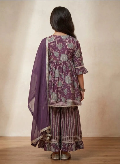 A woman shown from the back wearing a purple and silver floral printed kurta with matching striped palazzo pants and a sheer purple dupatta, set against a neutral beige background.