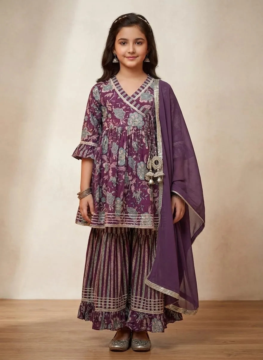 A young girl modeling a traditional Indian outfit consisting of a purple and gray patterned kurta, matching striped palazzo pants, and a solid purple dupatta, set against a neutral beige studio backdrop.