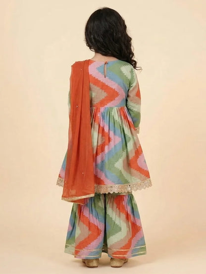 A child model shown from the back wearing a colorful chevron-patterned Anarkali suit with a solid orange dupatta, set against a plain beige studio background.