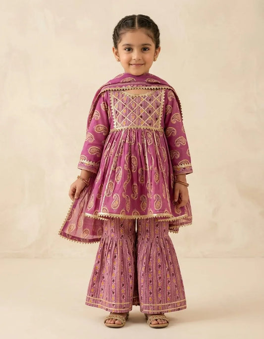 A young girl modeling a traditional Indian outfit consisting of a magenta pink kurta with gold embroidery, matching flared pants, and a dupatta, set against a plain beige background.