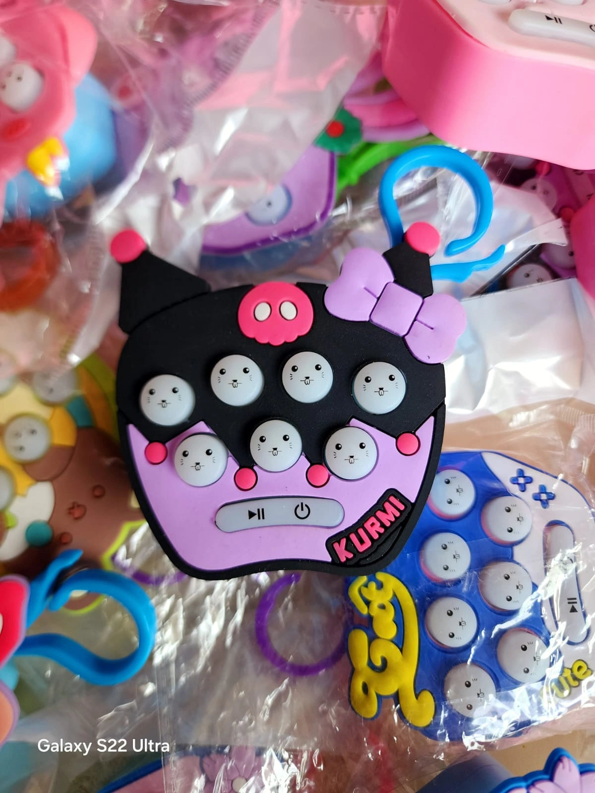 Close-up of a pink and black phone-shaped fidget toy with 'KURUMI' branding, surrounded by other toys.