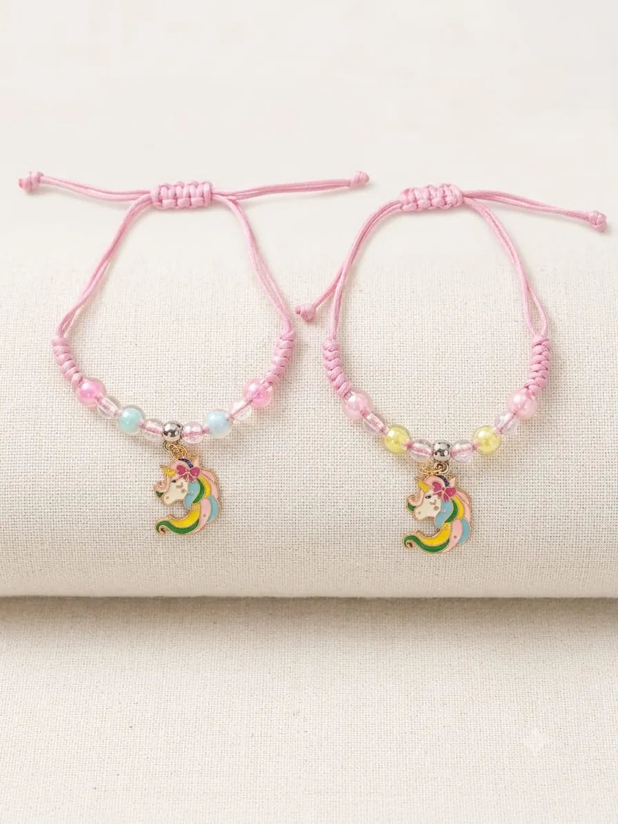 Two pink adjustable cord bracelets with small pastel beads and a dangling unicorn charm, displayed on a cream fabric surface.