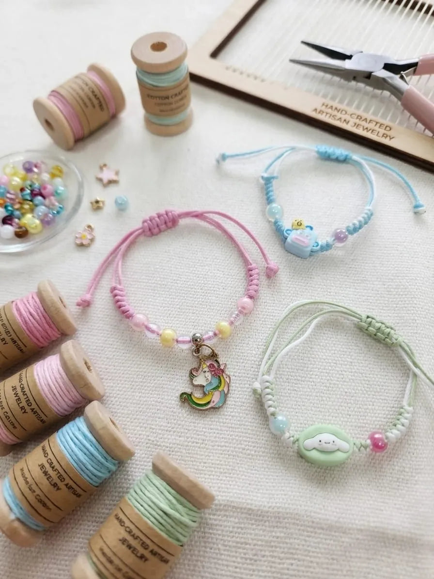 Three handmade cord bracelets with colorful beads and charms are arranged on a light fabric surface with spools of thread, beads, and a small wooden tray. A hand is partially visible holding a tool in the top right corner.