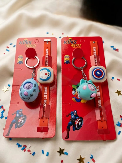Two packaged kids' superhero-themed keychains on red backing cards, displayed on a white fabric background with confetti and star decorations. One keychain has a blue round character charm and a white square charm, and the other has a teal cat-shaped charm and a white square charm with a Captain America shield.
