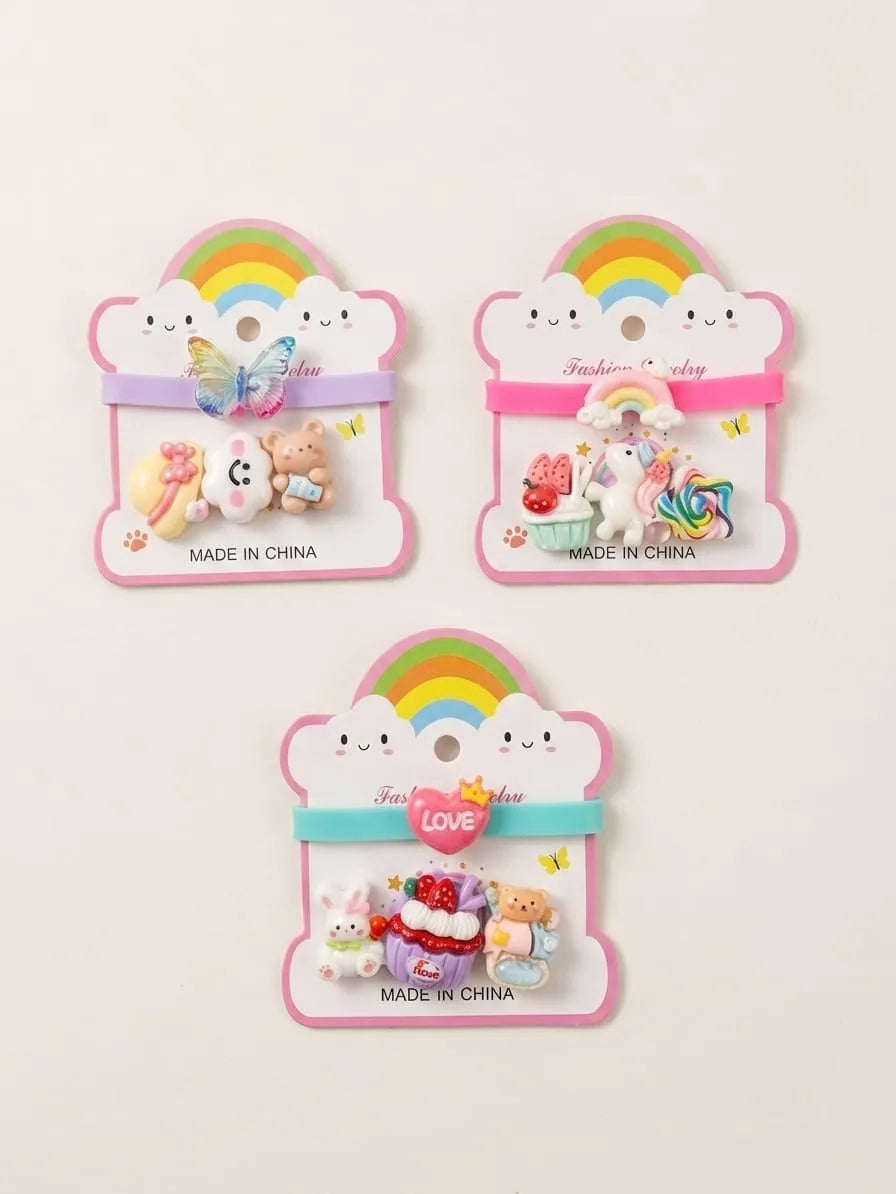 Three cute pastel hair clips displayed on pink cloud-shaped backing cards with rainbow graphics. The set includes a butterfly clip, a unicorn and cake clip, and a bunny and bear set, all labeled 'MADE IN CHINA'.