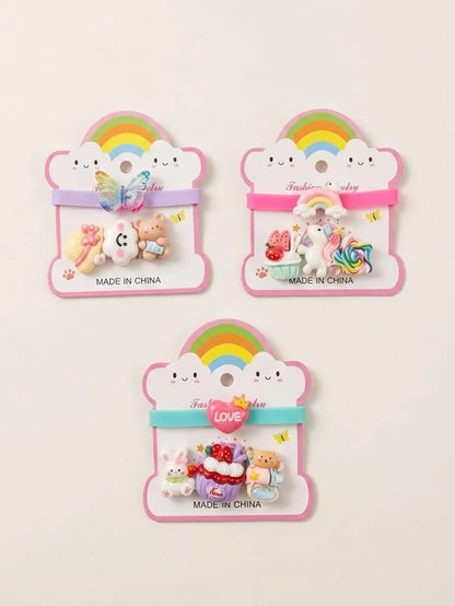 Three cute pastel hair clips displayed on pink cloud-shaped backing cards with rainbow graphics. The set includes a butterfly clip, a unicorn and cake clip, and a bunny and bear set, all labeled 'MADE IN CHINA'.