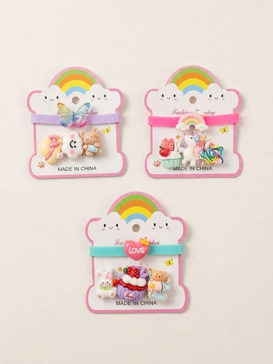 Three cute pastel hair clips displayed on pink cloud-shaped backing cards with rainbow graphics. The set includes a butterfly clip, a unicorn and cake clip, and a bunny and bear set, all labeled 'MADE IN CHINA'.