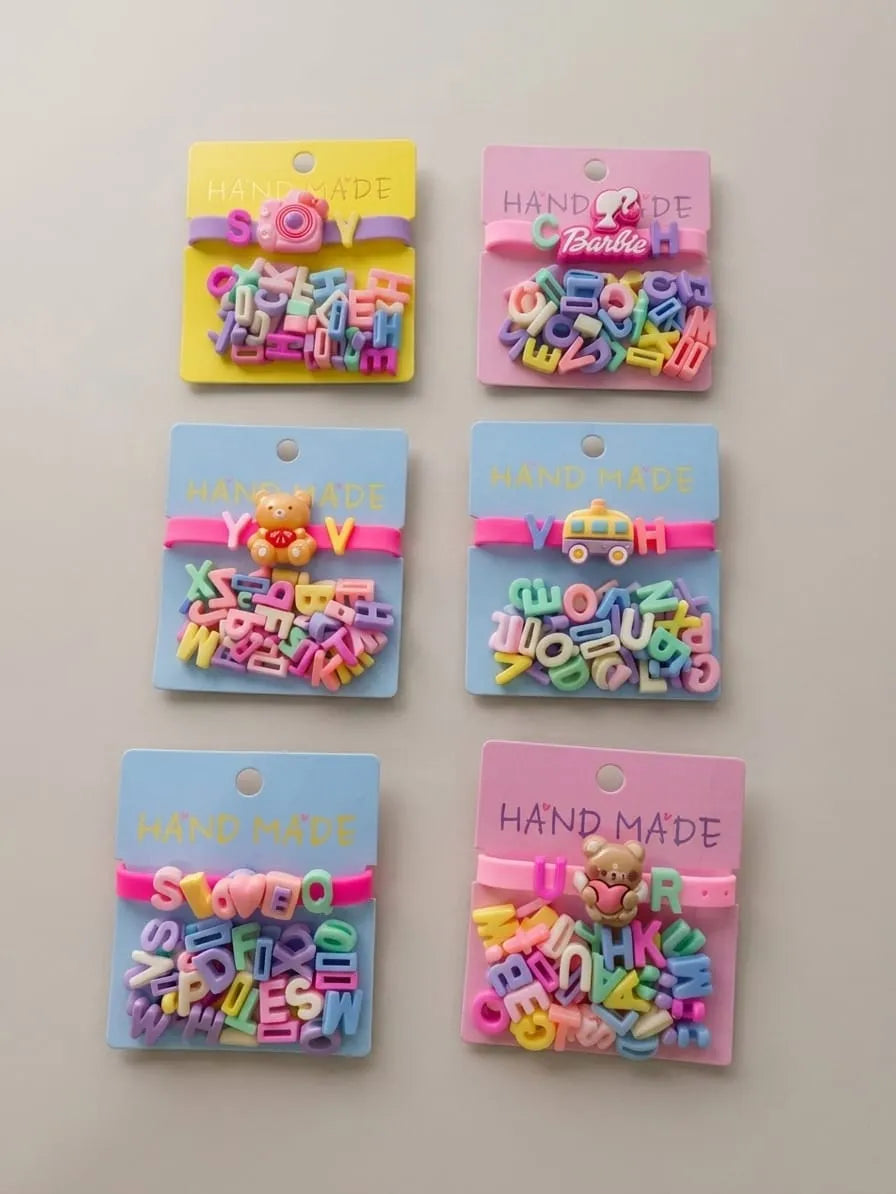 Six colorful handmade letter bead hair clips in various shapes and colors, each attached to a pastel-colored backing card with 'HAND MADE' printed on it, arranged in two columns of three on a light gray background.