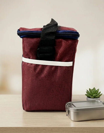 Maroon insulated lunch bag with black handle on a wooden surface with a plant in the background