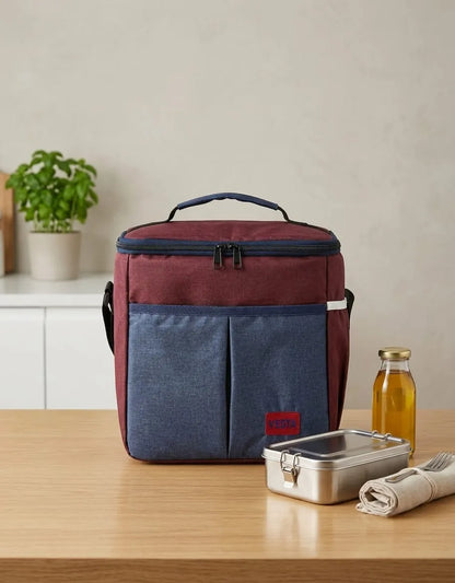 Maroon and blue cooler bag on a wooden table with a bottle and container.