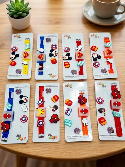 Eight colorful custom watch bands displayed on white cards on a wooden table, featuring various cartoon and superhero designs like Mickey Mouse, Spider-Man, Captain America, and Superman. A small potted succulent and a coffee cup are visible in the background.