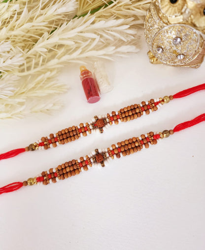 Two rudraksh rakhis with red strings and beadwork, displayed against a white background, alongside a small bottle and ornamental items.