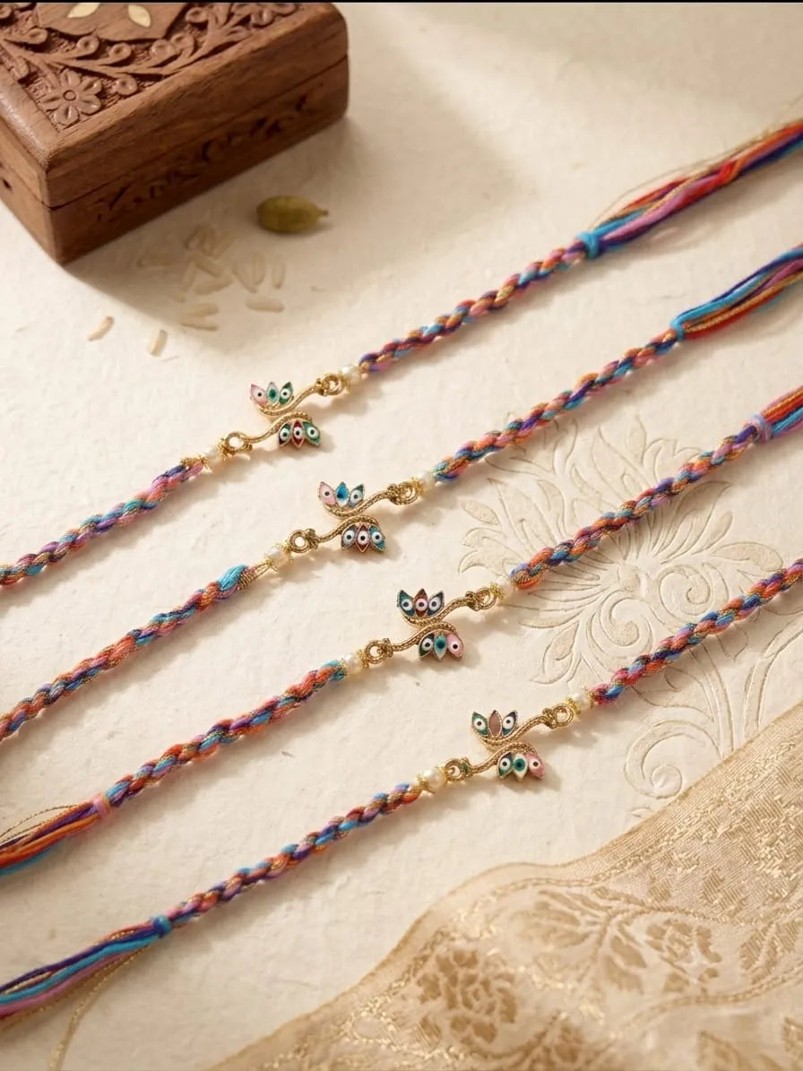 Four colorful braided Rakhi strands with small owl charms, arranged diagonally on a cream-colored textured surface with a carved wooden box in the background.