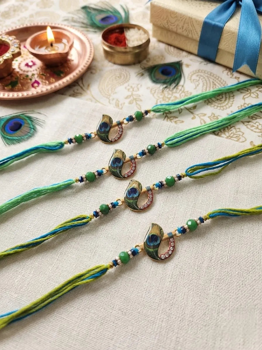 Three traditional Indian Rakhi beaded wristbands with peacock feather charms are displayed on a beige patterned fabric alongside festive props including a lit diya, a gift box, and peacock feather decorations.