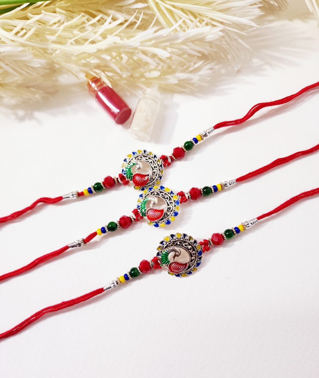 Two decorative necklaces with red strings and colorful beads on a textured white background