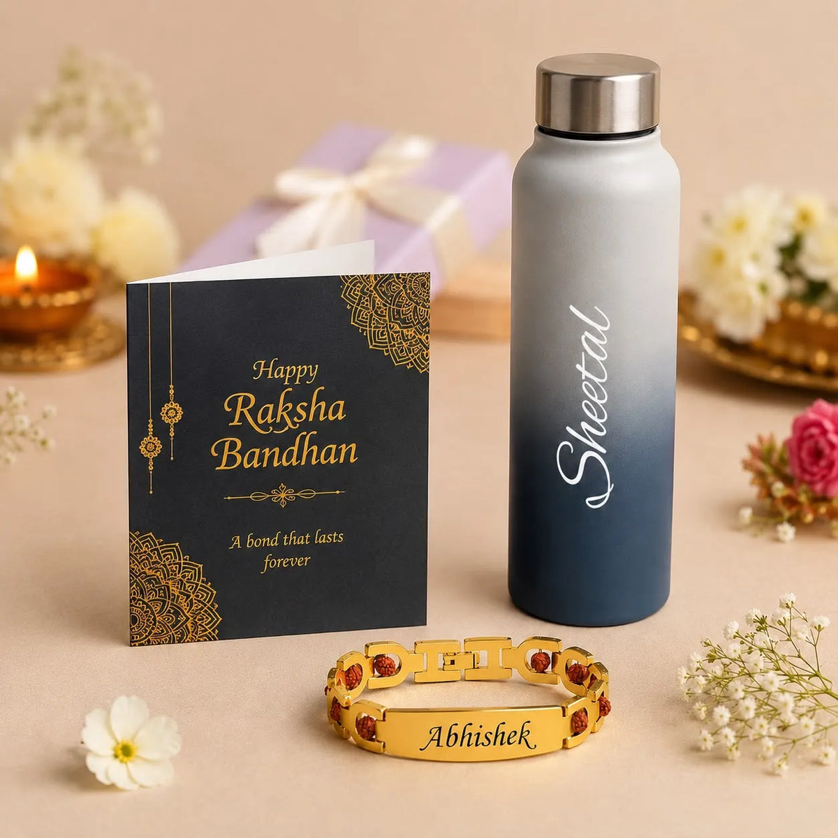 A personalized Raksha Bandhan gift set on a beige surface, featuring a gold-plated bracelet engraved with 'Abhishek' and red stones, a gray-to-blue gradient water bottle labeled 'Sheetal', and a black greeting card with gold text and mandala designs.