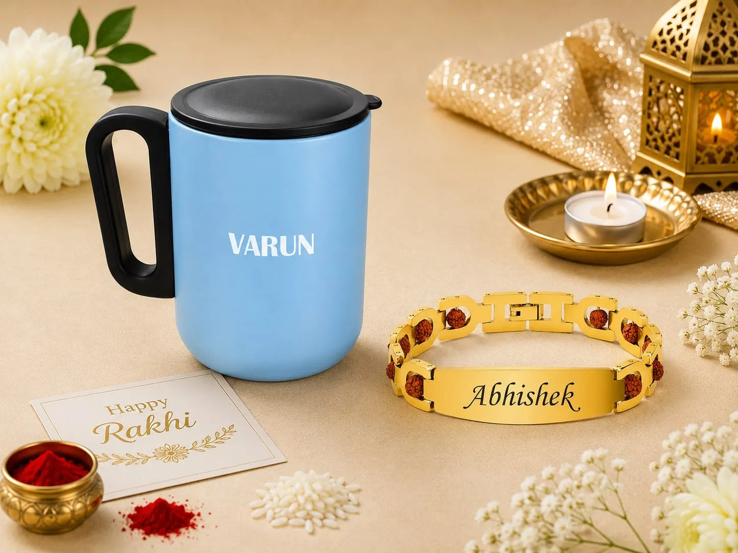 A personalized blue and black travel mug alongside a gold-plated Rakhi bracelet engraved with 'Abhishek' and accented with red stones, styled with festive props like flowers, a lit candle, and a greeting card on a beige background.