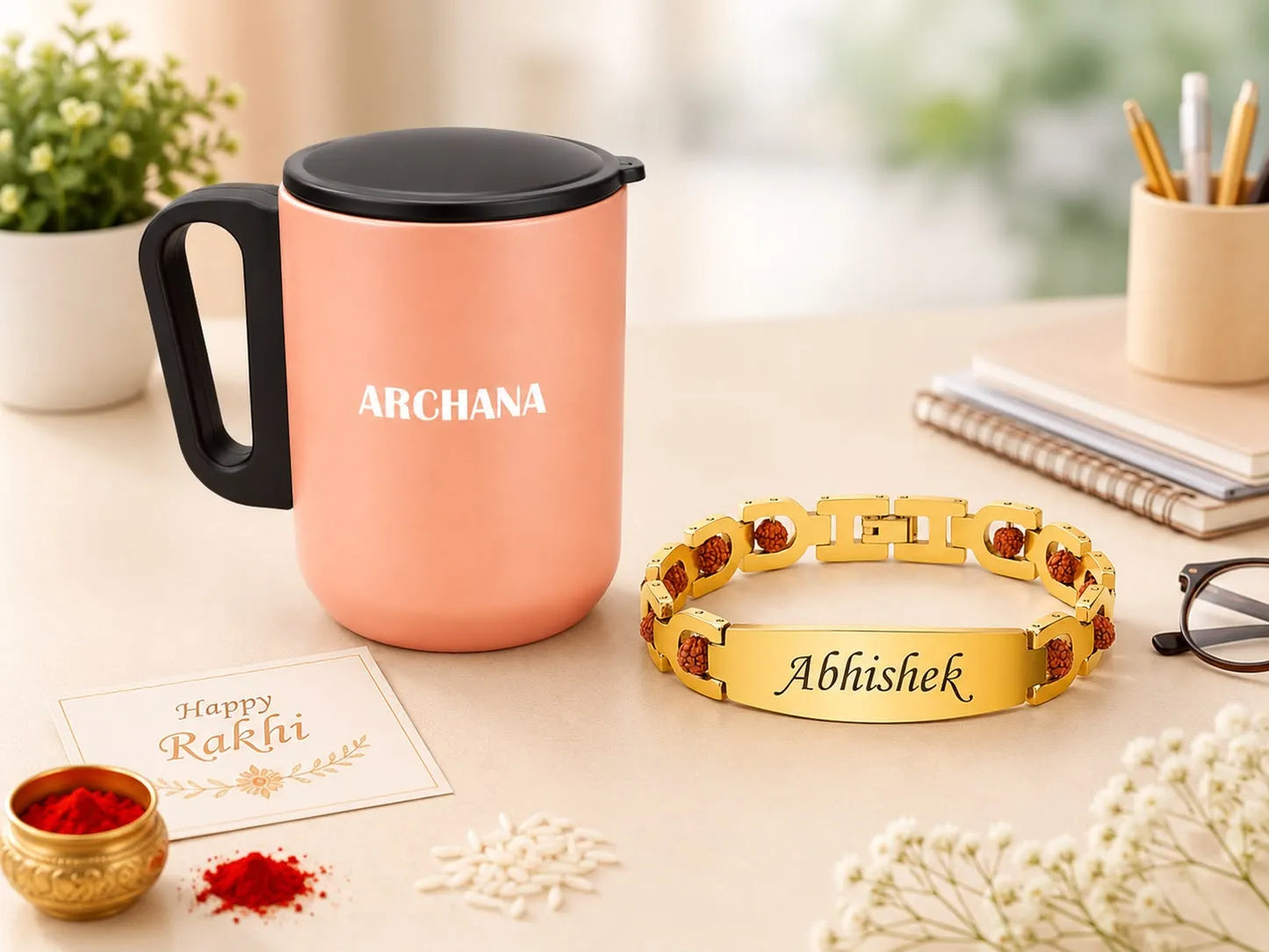 A styled Rakhi-themed scene showing a peach-colored insulated mug with a black lid and handle, alongside a gold-tone bracelet engraved with the names 'ARCHANA' and 'Abhishek'. The scene is decorated with a small card reading 'Happy Rakhi', red powder, white rice, glasses, and stationery on a light tabletop.