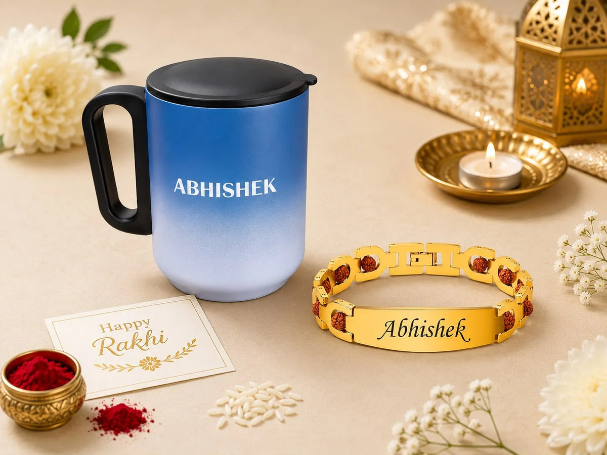 A blue-to-light-blue gradient insulated tumbler with a black handle and lid, alongside a gold-tone engraved bracelet both personalized with the name 'Abhishek'. The scene is styled for Rakhi with white flowers, red powder, a lit candle in a brass holder, and a greeting card on a beige background.