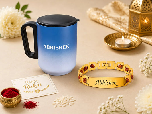 A blue-to-light-blue gradient insulated tumbler with a black handle and lid, alongside a gold-tone engraved bracelet both personalized with the name 'Abhishek'. The scene is styled for Rakhi with white flowers, red powder, a lit candle in a brass holder, and a greeting card on a beige background.