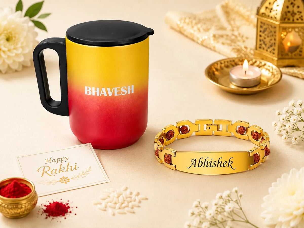 A festive product arrangement on a cream surface featuring a yellow-to-red gradient insulated tumbler with the name 'BHAVESH' printed on it, a gold-toned bracelet engraved with 'Abhishek' and accented with red stones, a small 'Happy Rakhi' card, red powder, white flowers, and a lit candle in a brass holder.